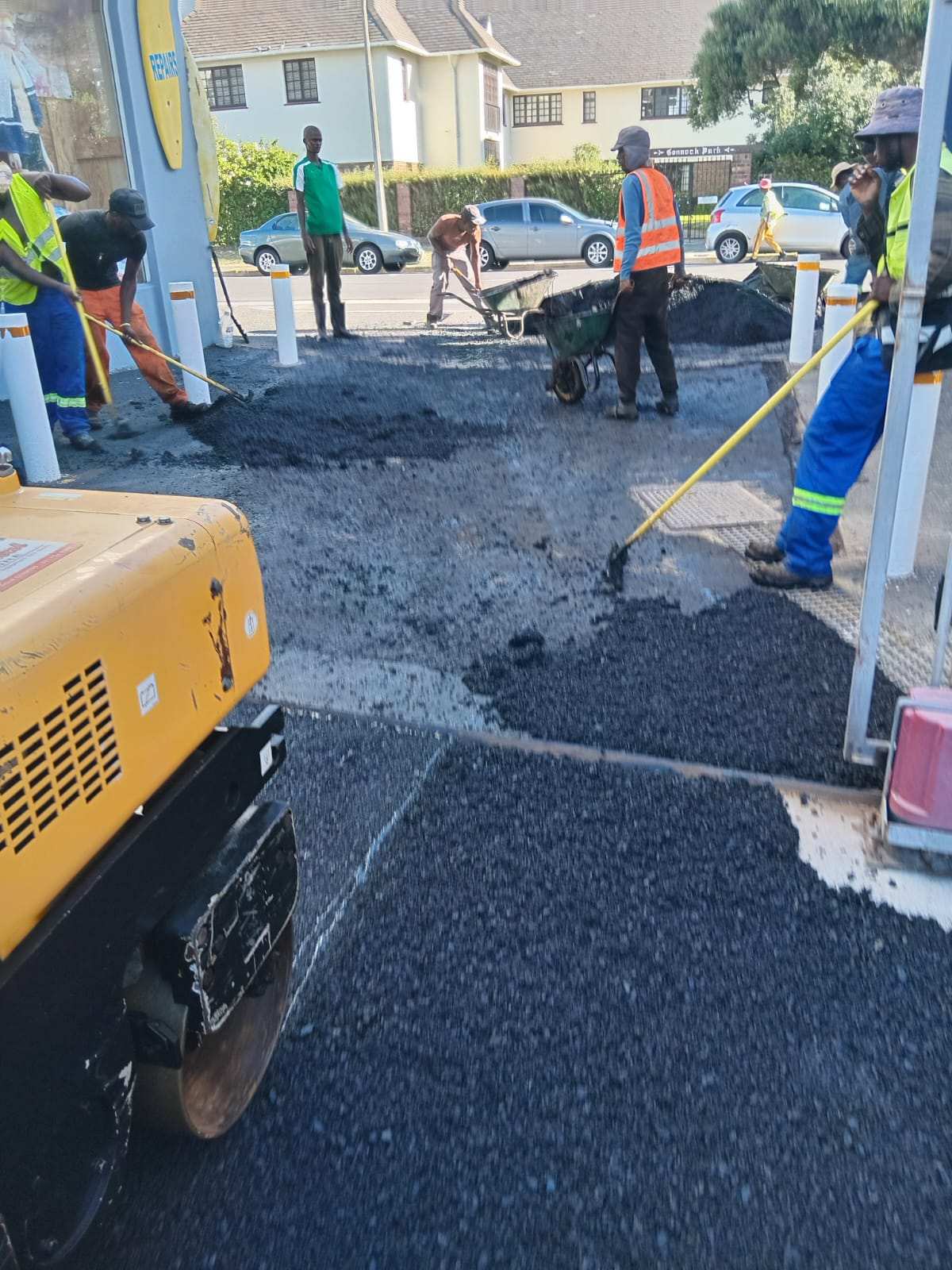 Crew placing hot asphalt into a cut-out repair beside a mini excavator