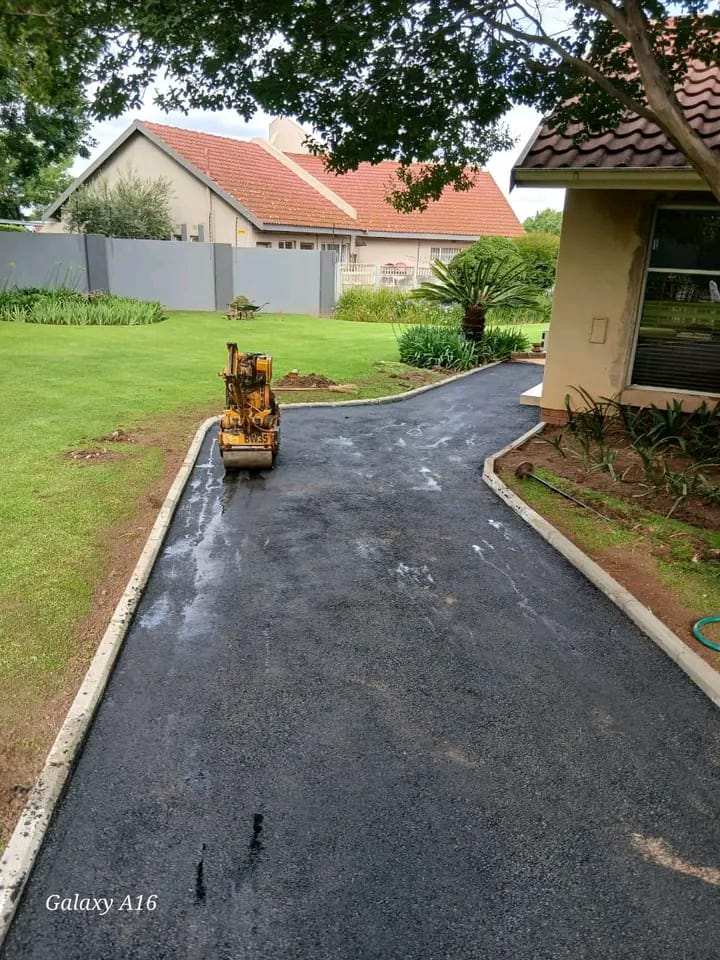 New tar driveway edged with concrete kerbs, curving through a lawn, with a small roller on the drive