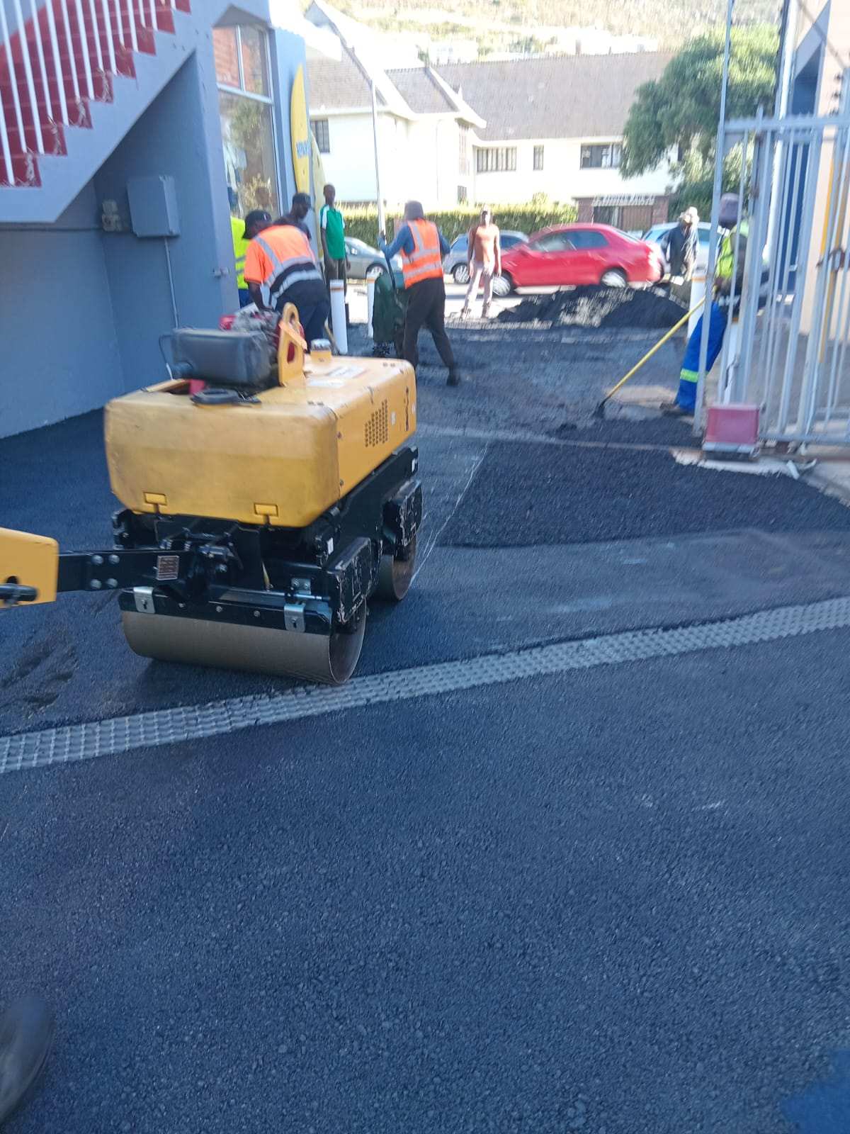 Pedestrian roller compacting new asphalt beside a channel drain