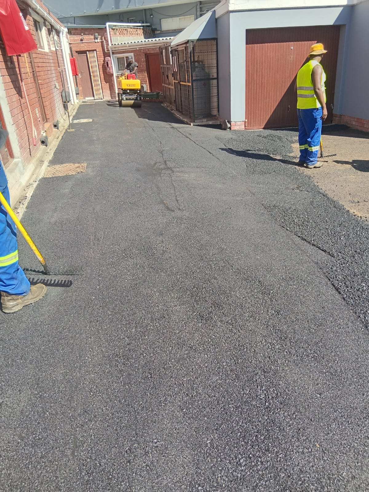 Worker levelling hot asphalt with a rake along a driveway