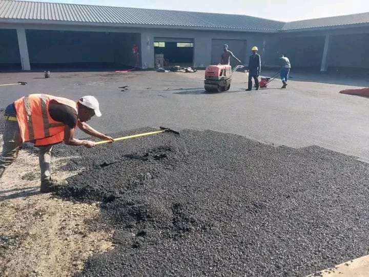 Crew member spreading hot asphalt with a rake in a commercial yard