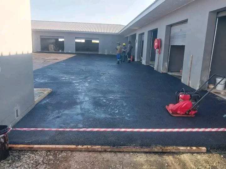 Freshly surfaced yard in front of industrial units, with a plate compactor on the new asphalt